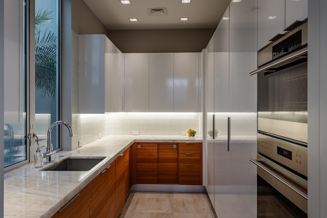 kitchen featuring light stone counters, white cabinetry, sink, and tasteful backsplash