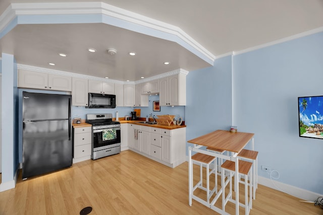 kitchen with black appliances, light wood-type flooring, white cabinetry, and wooden counters