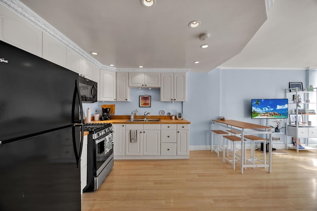 kitchen featuring sink, wooden counters, light hardwood / wood-style floors, white cabinets, and black appliances