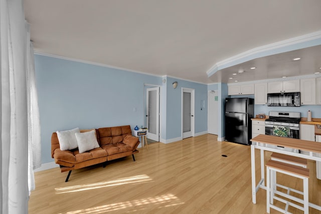 kitchen with light hardwood / wood-style flooring, white cabinetry, ornamental molding, and black appliances