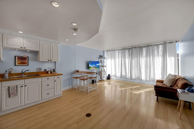 interior space featuring butcher block counters, white cabinetry, sink, and light hardwood / wood-style flooring