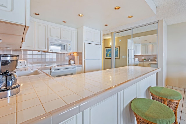 kitchen with decorative backsplash, white cabinets, tile countertops, and white appliances