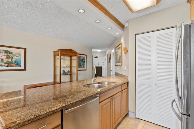 kitchen featuring sink, dark stone counters, a textured ceiling, light tile patterned floors, and appliances with stainless steel finishes