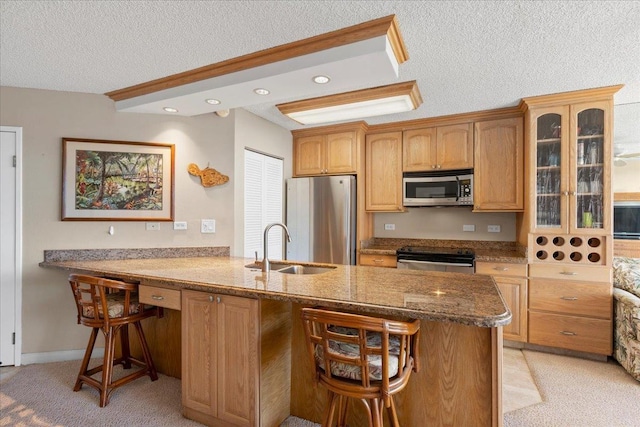 kitchen with sink, a textured ceiling, stone countertops, a kitchen bar, and stainless steel appliances