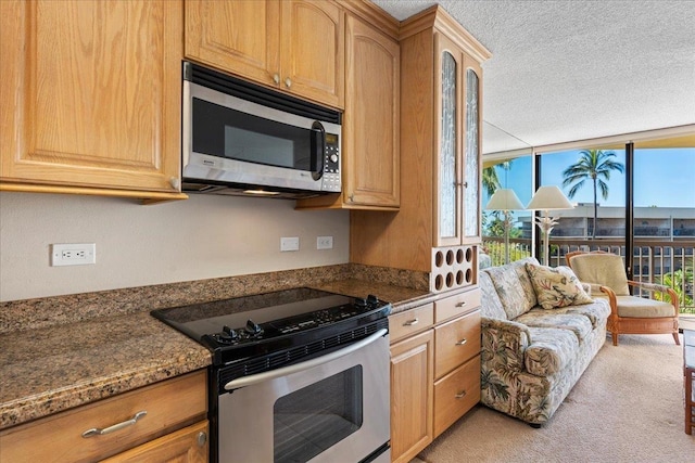 kitchen with a textured ceiling, stainless steel appliances, dark stone counters, and light colored carpet