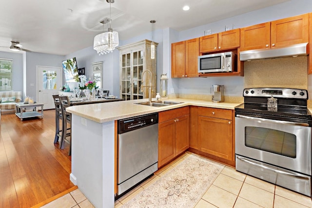 kitchen featuring ceiling fan with notable chandelier, light hardwood / wood-style flooring, appliances with stainless steel finishes, kitchen peninsula, and sink