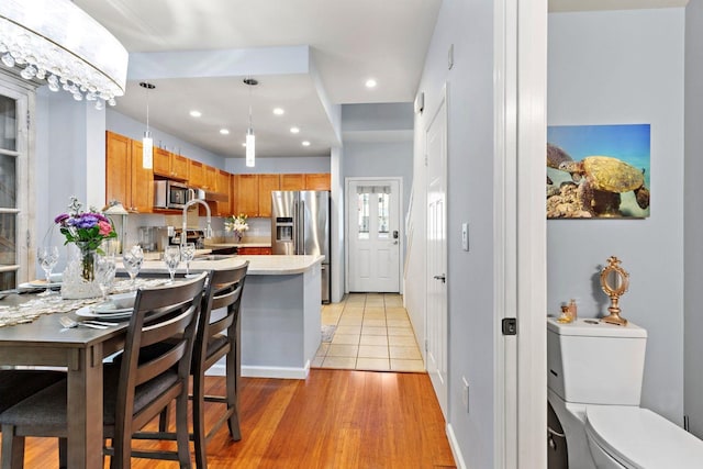 kitchen with light wood-type flooring, kitchen peninsula, sink, hanging light fixtures, and appliances with stainless steel finishes