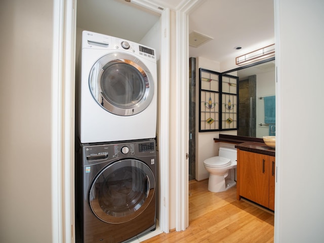 clothes washing area with stacked washing maching and dryer and light hardwood / wood-style flooring