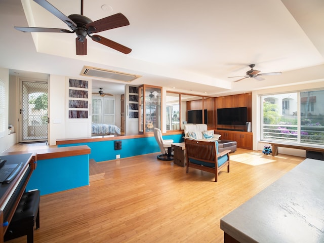 living room featuring ceiling fan, a tray ceiling, plenty of natural light, and light hardwood / wood-style flooring