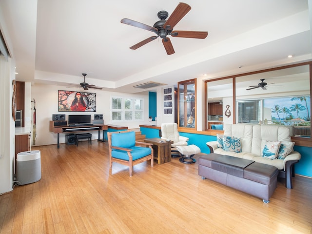 living room with light wood-type flooring, a raised ceiling, and ceiling fan