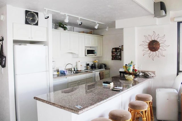 kitchen with white appliances, a breakfast bar area, dark stone countertops, a peninsula, and a sink