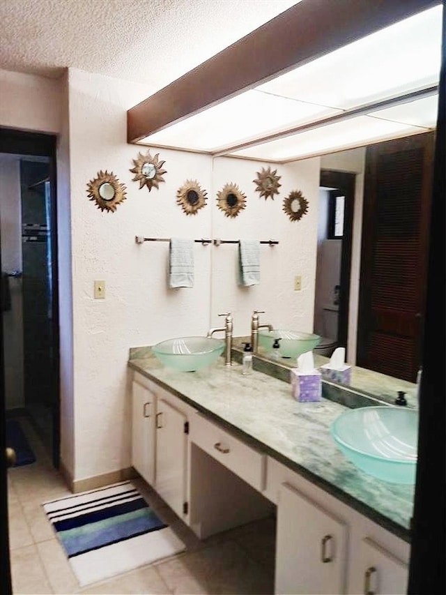 full bath with a textured ceiling, double vanity, tile patterned flooring, and a sink