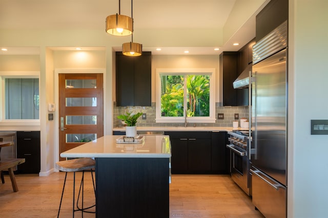 kitchen featuring light countertops, under cabinet range hood, a sink, light wood-style flooring, and premium appliances