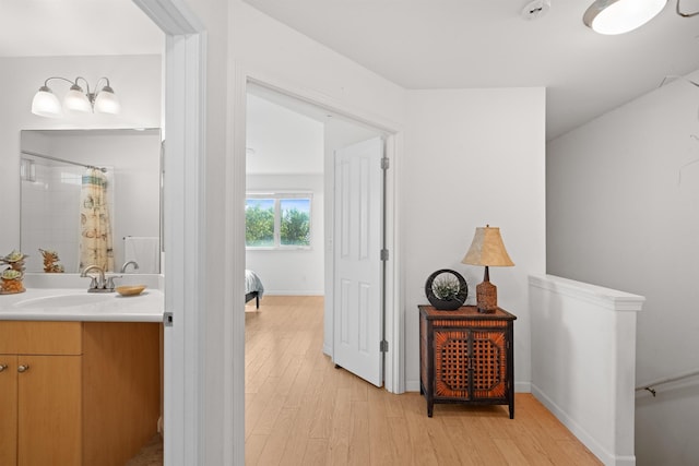 hallway with a sink, light wood-style flooring, and baseboards