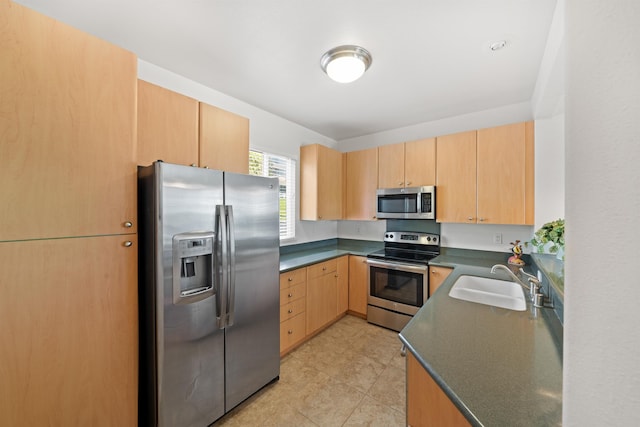 kitchen featuring stainless steel appliances, a sink, dark countertops, and light brown cabinetry