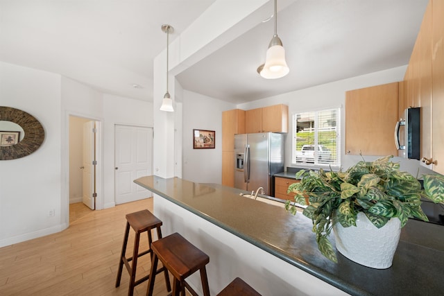 kitchen featuring appliances with stainless steel finishes, a peninsula, dark countertops, a sink, and a kitchen breakfast bar
