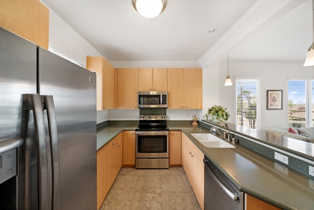 kitchen featuring appliances with stainless steel finishes, a sink, light brown cabinets, dark countertops, and a peninsula