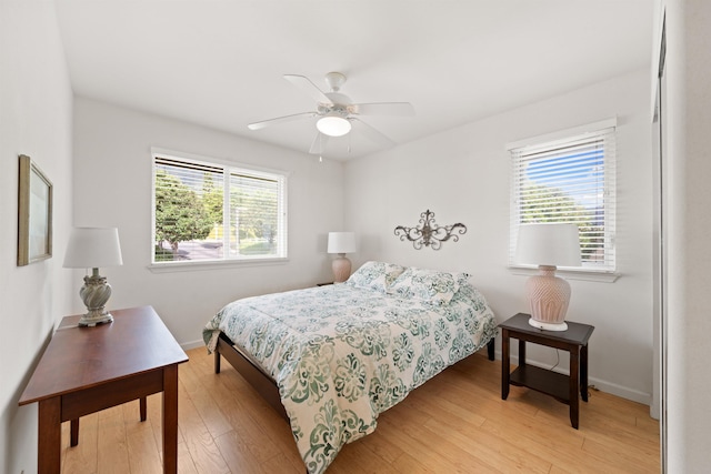 bedroom with multiple windows, light wood-style flooring, baseboards, and a ceiling fan