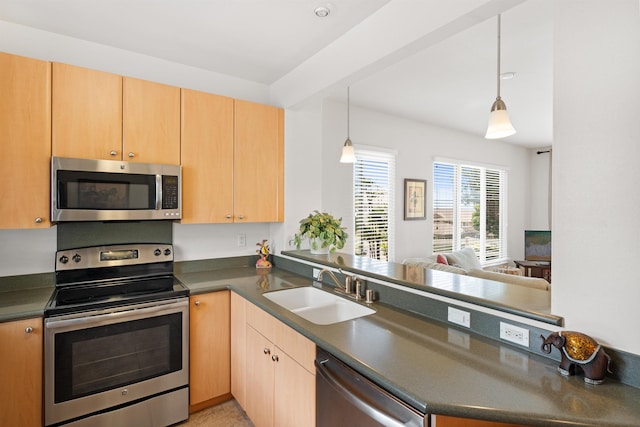 kitchen featuring stainless steel appliances, a sink, dark countertops, a peninsula, and light brown cabinetry