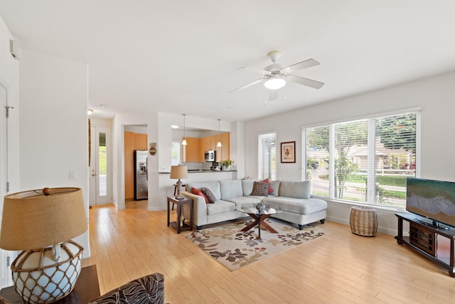 living area with a ceiling fan, light wood-style flooring, and baseboards