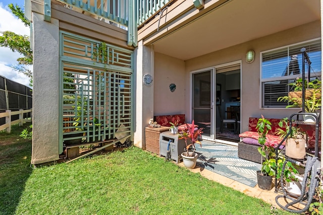 view of exterior entry featuring a patio, a yard, fence, and stucco siding