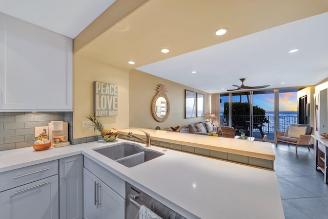 kitchen featuring a sink, backsplash, open floor plan, a peninsula, and light countertops