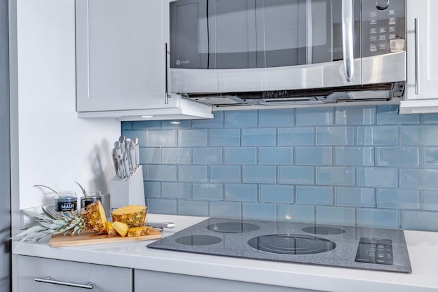 kitchen featuring stainless steel microwave, backsplash, white cabinets, light countertops, and black electric cooktop