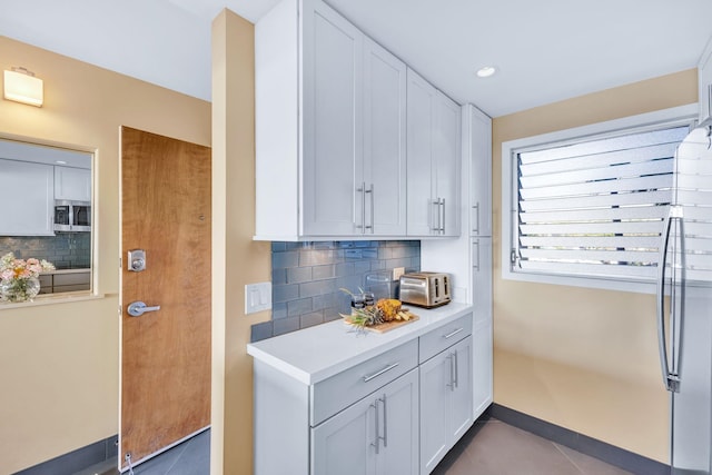 kitchen with stainless steel microwave, light countertops, decorative backsplash, and dark tile patterned flooring