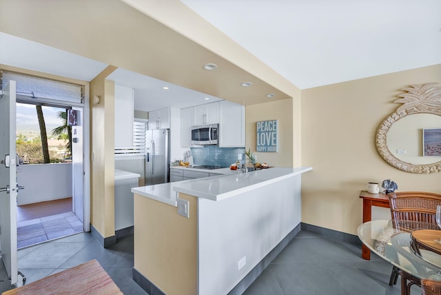 kitchen featuring a peninsula, dark tile patterned flooring, decorative backsplash, white cabinets, and appliances with stainless steel finishes