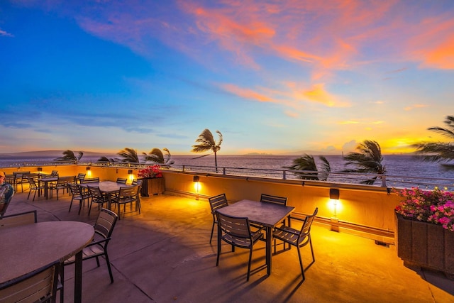 patio terrace at dusk featuring visible vents, outdoor dining area, and a water view