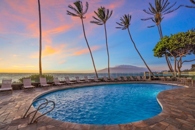 pool at dusk featuring a patio area and a community pool