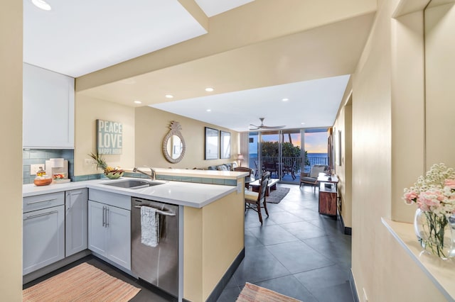 kitchen featuring light countertops, decorative backsplash, a peninsula, stainless steel dishwasher, and a sink