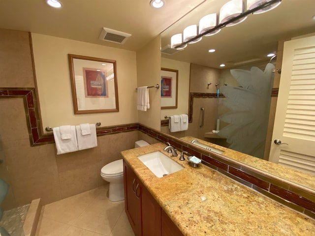 bathroom featuring a shower with door, vanity, tile patterned flooring, tile walls, and toilet