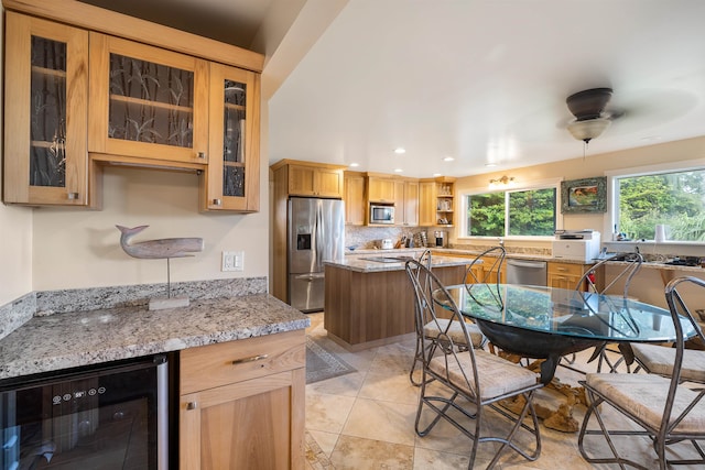 kitchen with backsplash, ceiling fan, light stone counters, stainless steel appliances, and beverage cooler