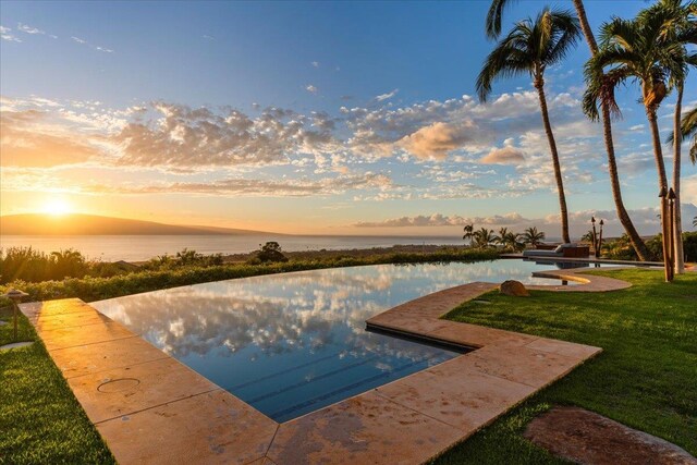 pool at dusk featuring a yard and a water view