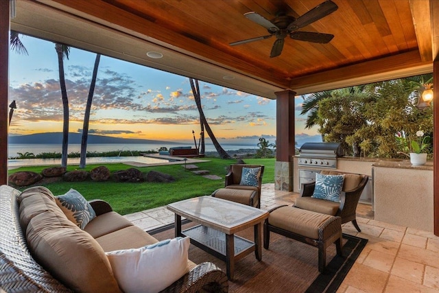 patio terrace at dusk with a yard, a grill, exterior kitchen, outdoor lounge area, and ceiling fan