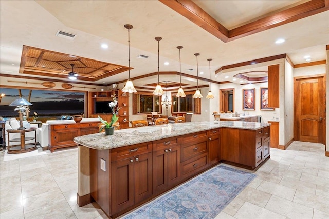 kitchen with a large island, light stone counters, pendant lighting, and a raised ceiling