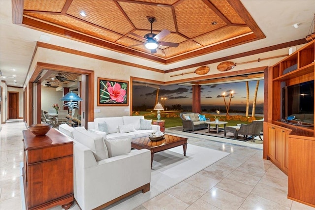 living room with ornamental molding, a tray ceiling, light tile patterned floors, and ceiling fan