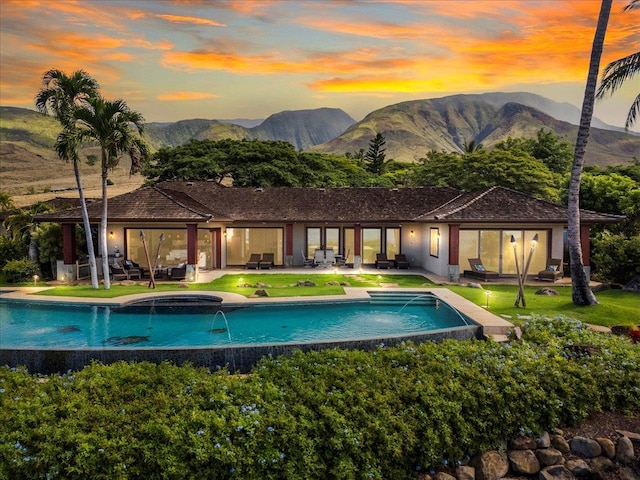 pool at dusk with an in ground hot tub, a patio, pool water feature, and a mountain view