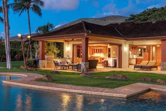 back house at dusk featuring a yard, an outdoor living space, area for grilling, and ceiling fan