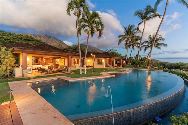 pool at dusk with a patio, a mountain view, pool water feature, and an outdoor hangout area