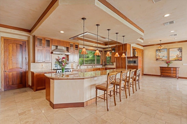 kitchen with a spacious island, wall chimney exhaust hood, light stone countertops, decorative light fixtures, and appliances with stainless steel finishes