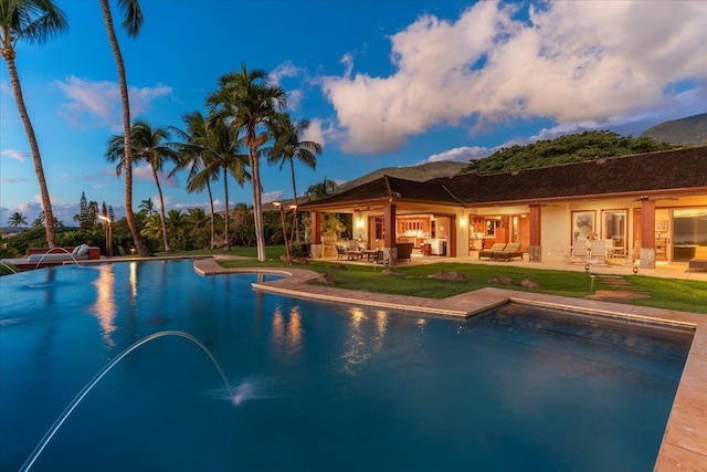 pool at dusk with a patio, outdoor lounge area, and pool water feature