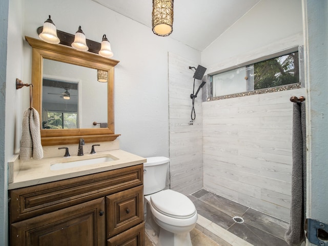 bathroom with toilet, vaulted ceiling, a tile shower, ceiling fan, and vanity