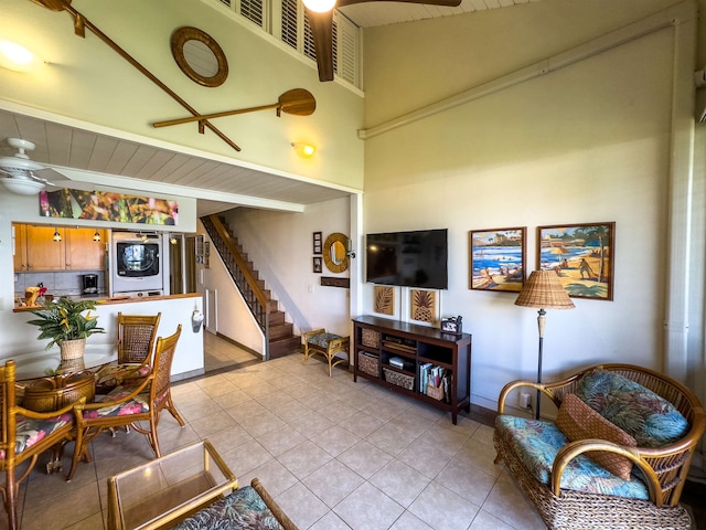 living room featuring stacked washer and clothes dryer, a towering ceiling, ceiling fan, and light tile patterned flooring