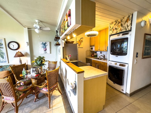 kitchen with stacked washing maching and dryer, stainless steel fridge, black electric cooktop, sink, and light tile patterned floors