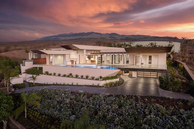 back house at dusk with a mountain view, a balcony, and a patio area