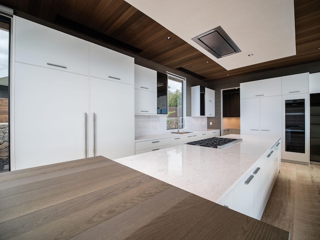 kitchen featuring tasteful backsplash, light wood-type flooring, light stone counters, white cabinetry, and wooden ceiling