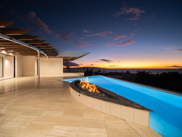 pool at dusk featuring an outdoor fire pit and a patio area