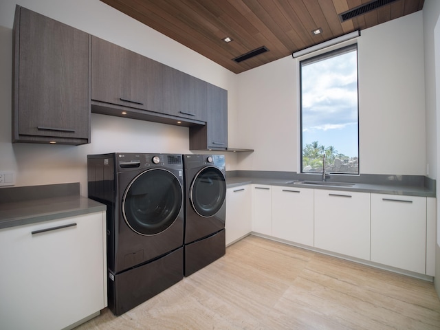 clothes washing area featuring light hardwood / wood-style floors, wood ceiling, washing machine and dryer, sink, and cabinets